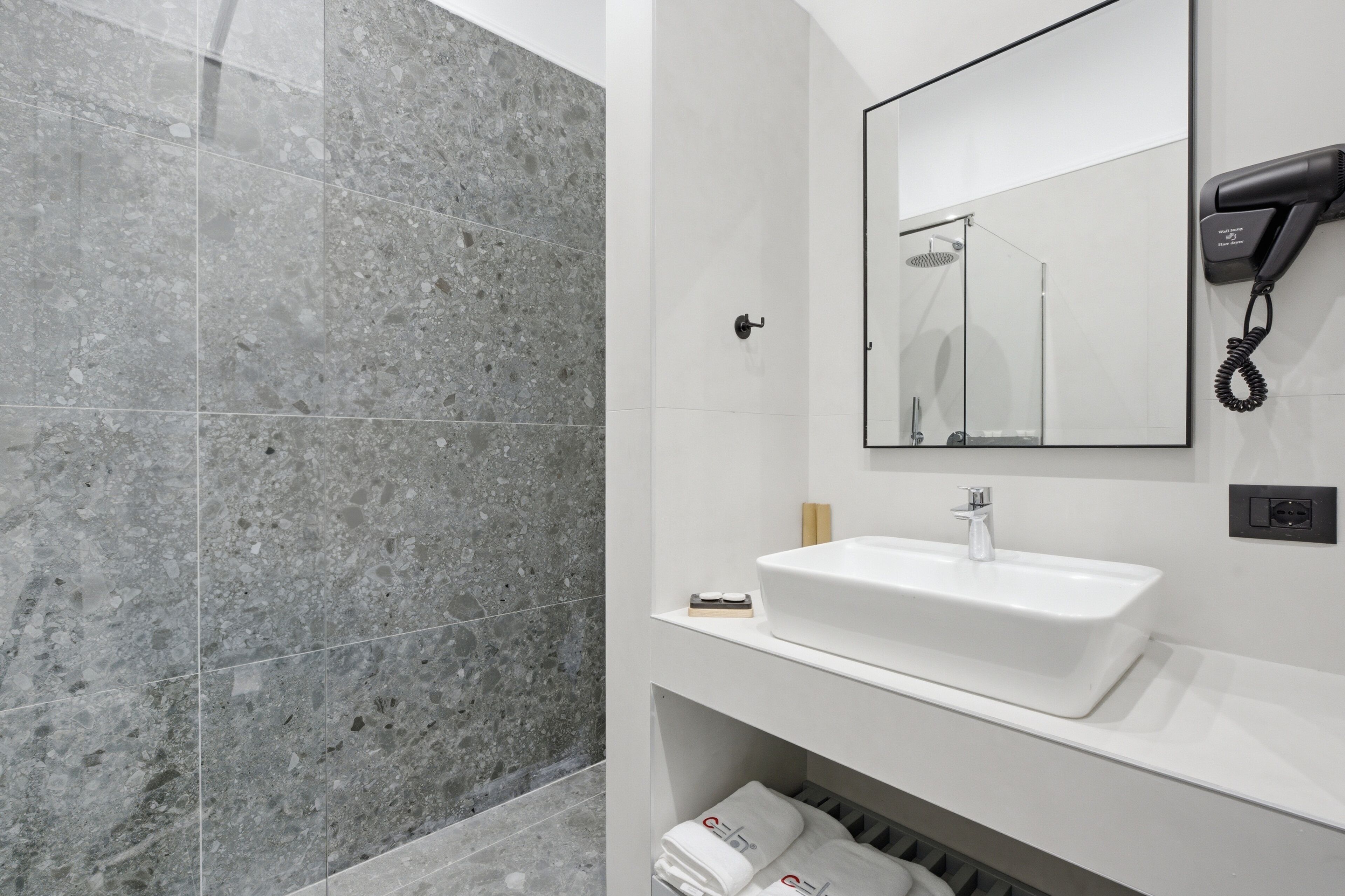 Een moderne badkamer met een wit wastafelmeubel, een haardroger en een douchehoek.