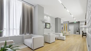 A modern hotel lobby with white sofas, a dining area, and a large window with curtains. - Cela Hotel (Durrës)