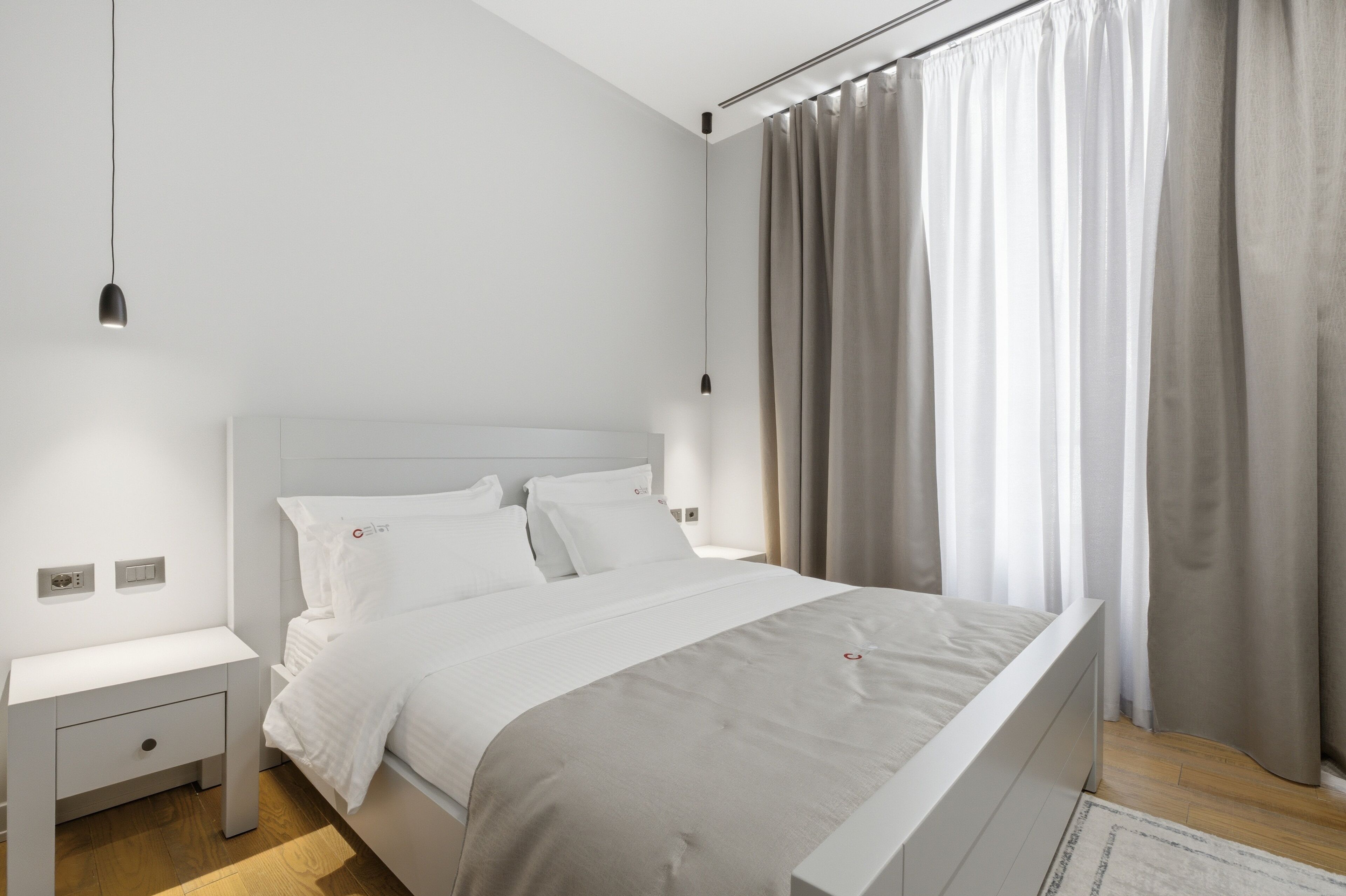 Un dormitorio moderno con una cama blanca, una mesita de noche y una lámpara colgante.