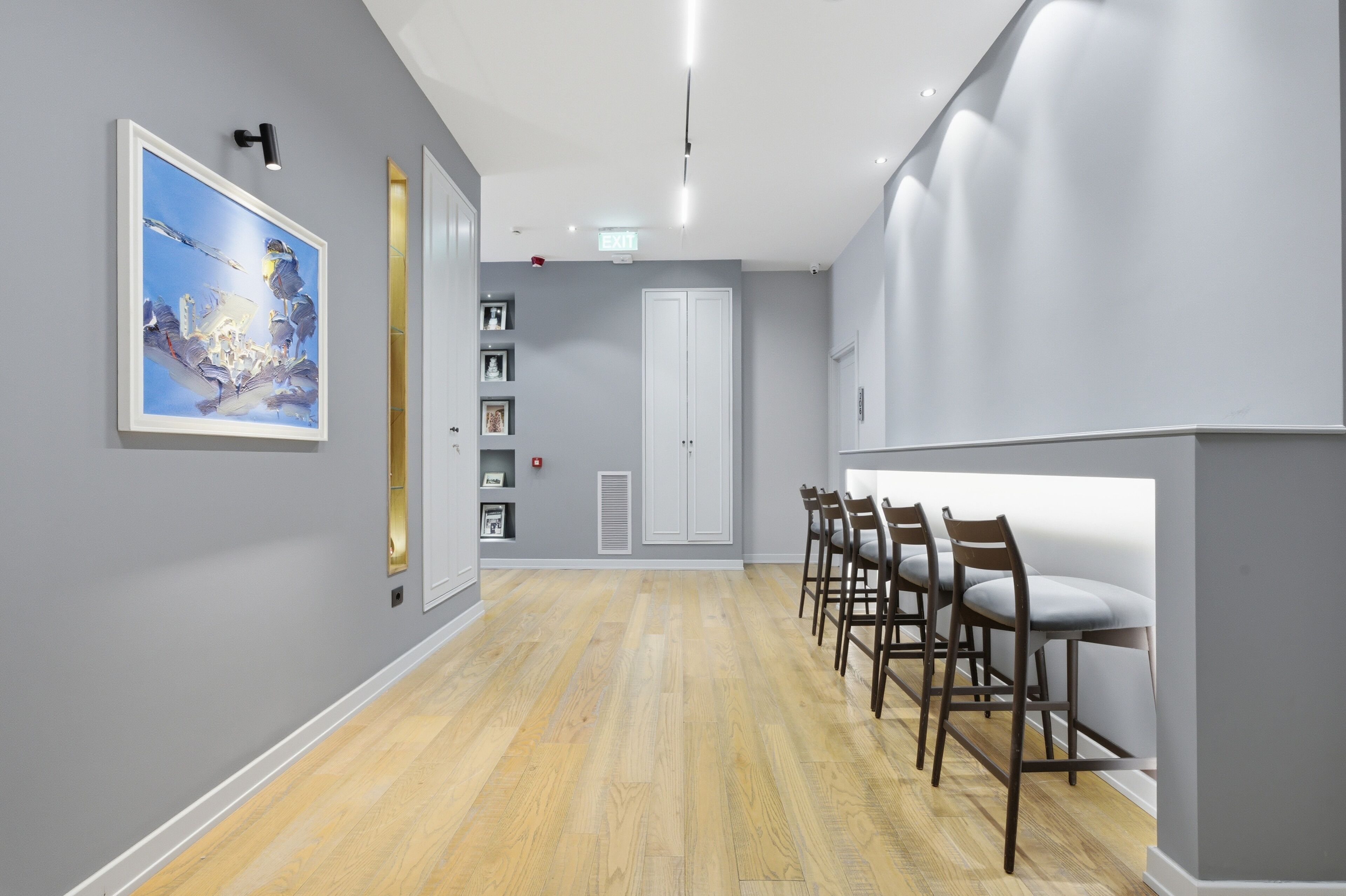 Un pasillo con piso de madera, un mostrador de recepción con taburetes de bar, una obra de arte enmarcada en la pared y una puerta con marco blanco.