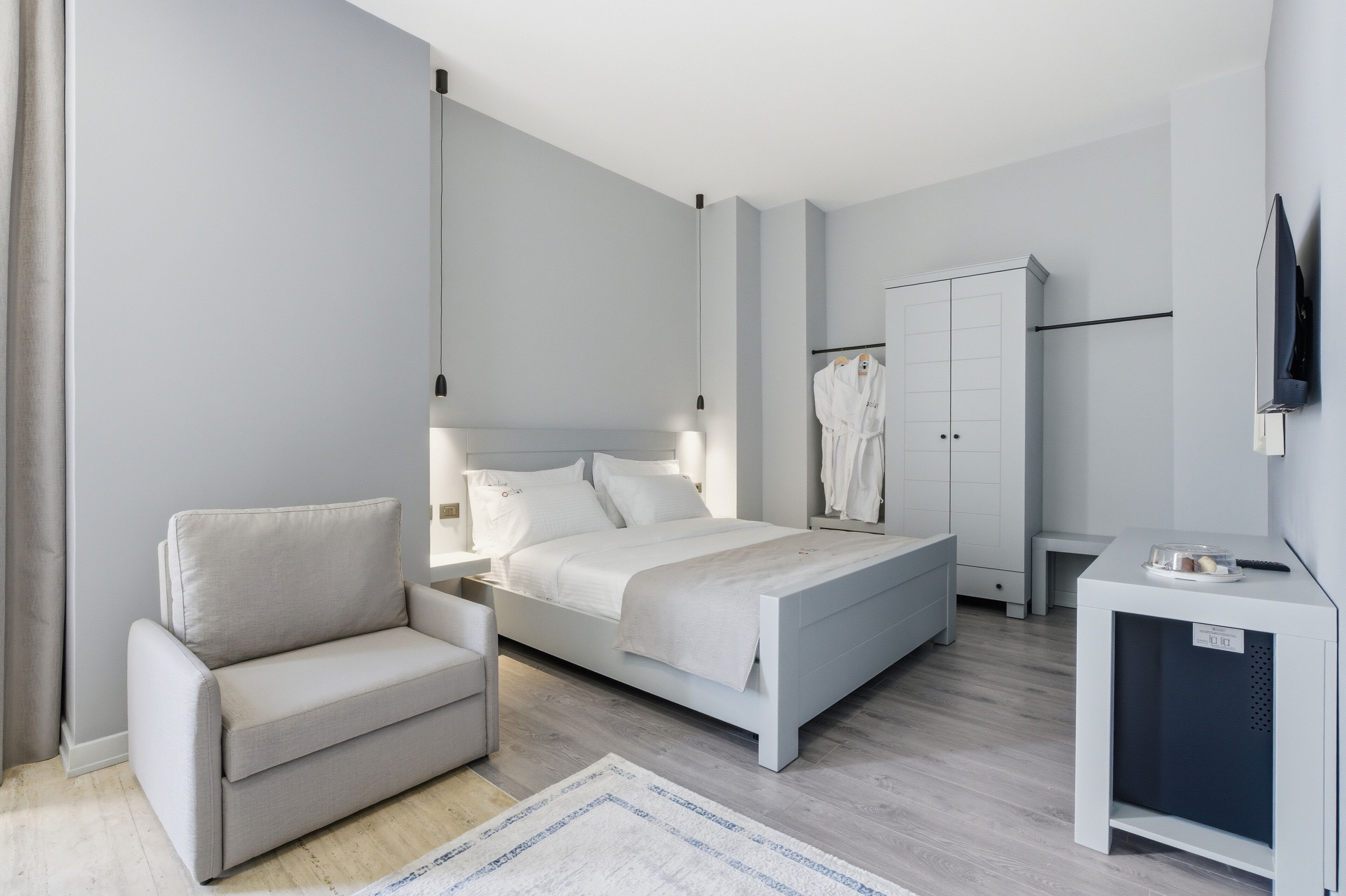 A modern bedroom with a bed, a chair, a wardrobe, and a TV.