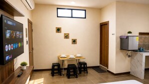 Habitación de hotel con cama, televisor montado en la pared, una pequeña mesa con taburetes, escritorio y refrigerador.