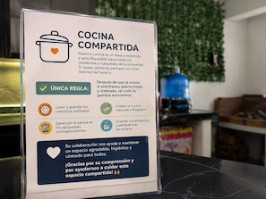 Un cartel detalla las normas de la cocina compartida, como limpiar los utensilios, desechar la basura y guardar alimentos y objetos personales.