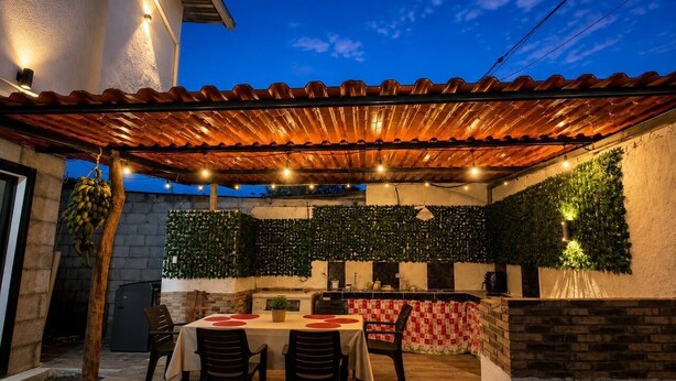 Un patio exterior con mesa y sillas, un muro de ladrillo con vegetación y un tejado de baldosas.