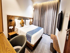 A hotel room with a bed, a chair, a bedside table, a TV, and a curtain.