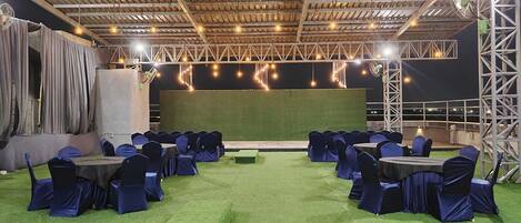 An indoor event space with a stage, rows of tables with chairs, and a green carpet.