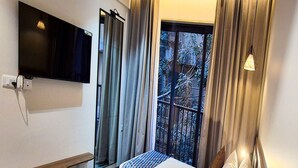 Une chambre d’hôtel avec deux lits, un téléviseur fixé au mur, une fenêtre avec des rideaux et une étagère en bois.