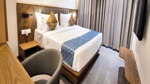 Une chambre d’hôtel avec un lit, un bureau, une chaise, une télévision et une fenêtre avec des rideaux.