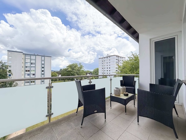 A balcony with wicker furniture, a tiled floor, and a view of buildings and trees. - Bright Designer Home | Terrace & 2xFree Parking (Bayreuth)