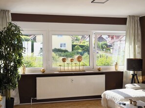Ein Schlafzimmer mit großem Fenster, Heizkörper, Bett, Nachttisch und Lampe.