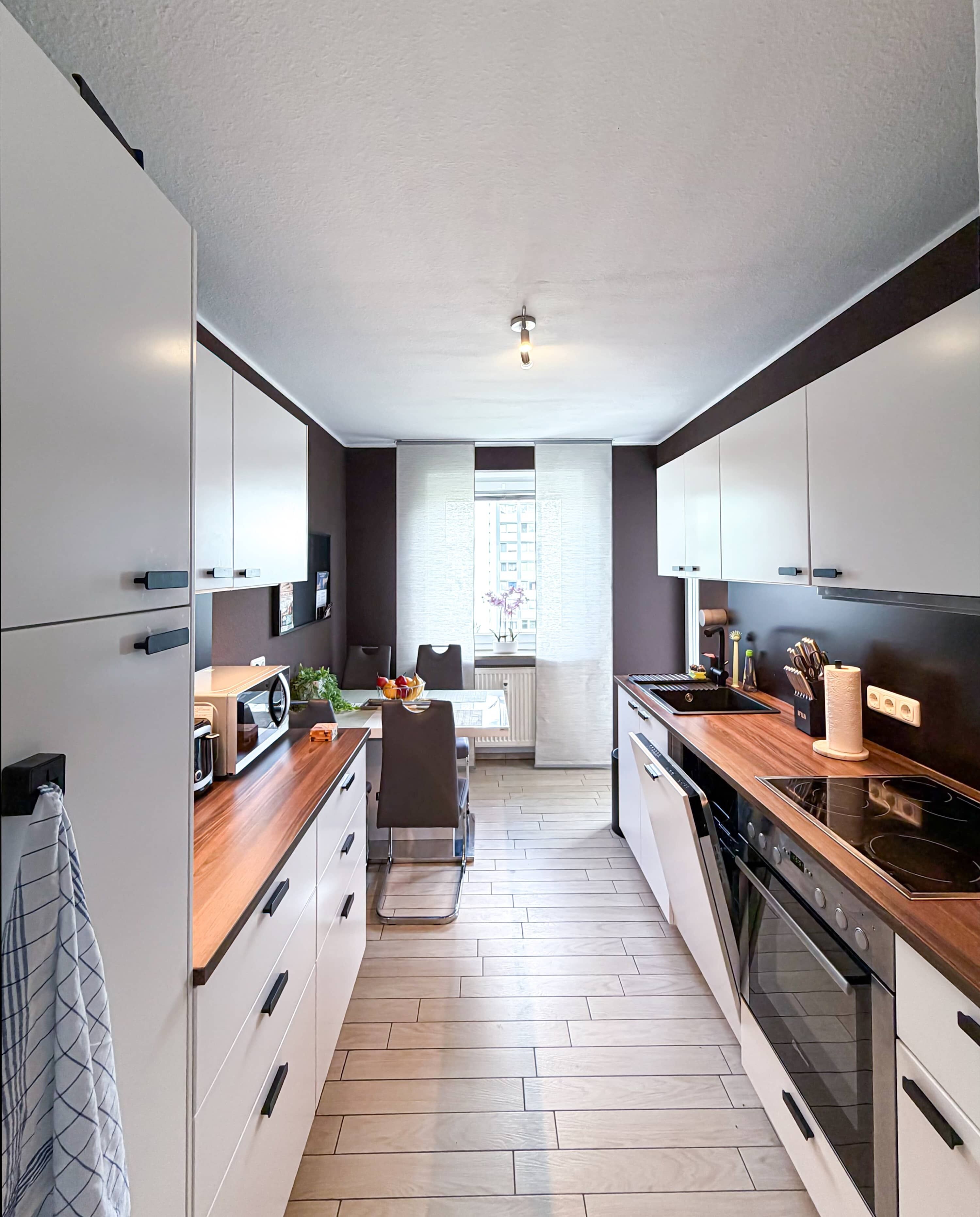 A modern kitchen with white cabinets, a wooden countertop, a built-in oven, and a dining area with a table and chairs.