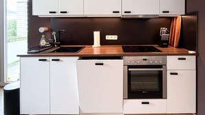 Uma cozinha moderna com armários brancos, bancada de madeira, forno embutido e janela com vista para o verde.