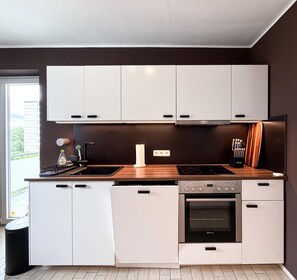 Eine moderne Küche mit weißen Schränken, einer Holzarbeitsplatte, einem eingebauten Backofen und einem Fenster mit Blick auf Grünflächen.
