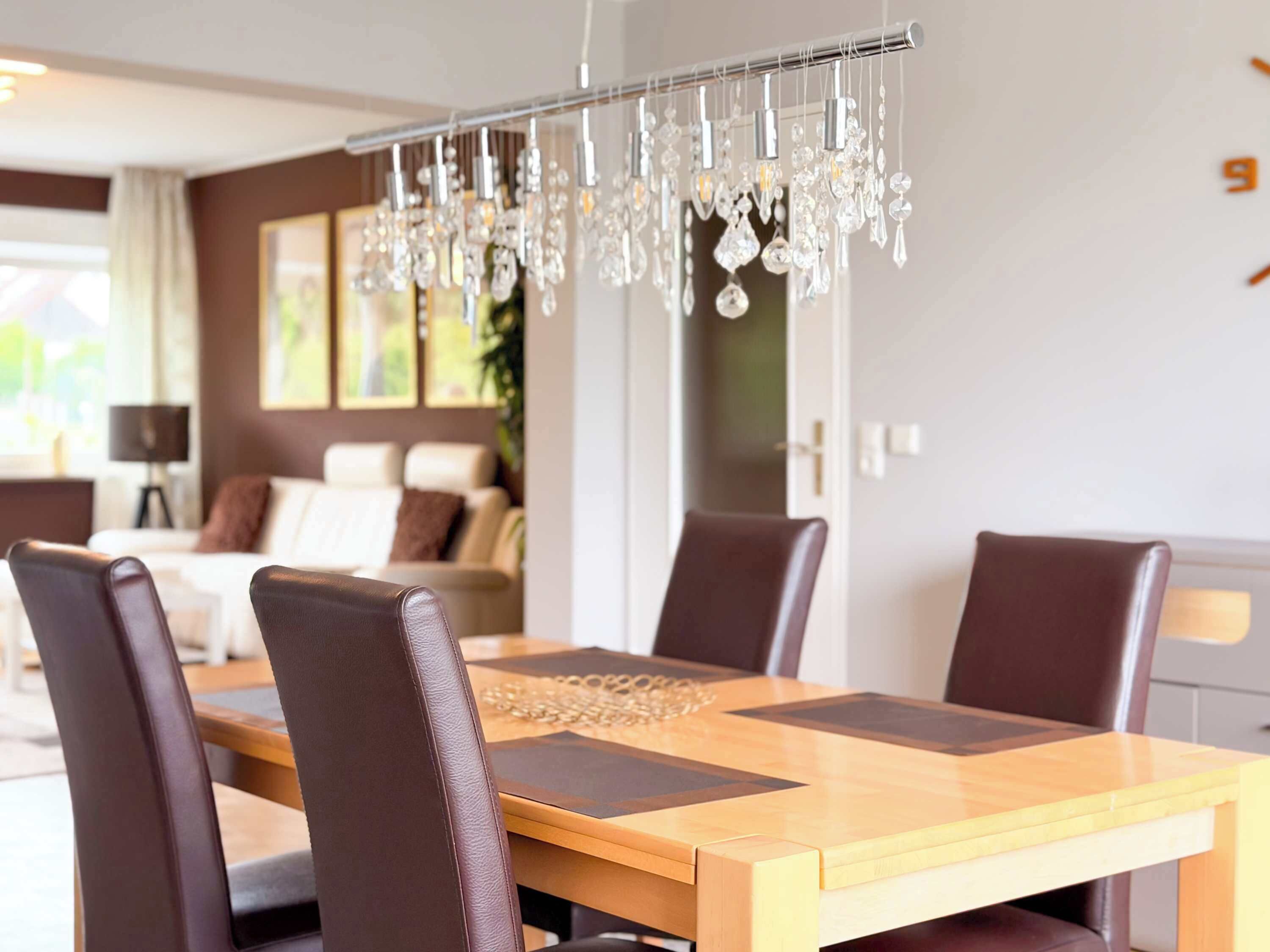 A dining area with a wooden table, brown leather chairs, and a chandelier.