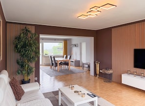 A modern living room with a dining area, a large potted plant, and a flat-screen TV on a wall. - Bright Designer Home | Terrace & 2xFree Parking (Bayreuth)