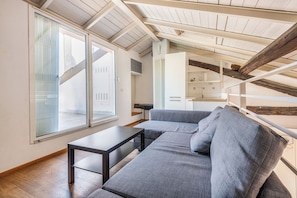 A modern loft bedroom with a sloped ceiling, a built-in sofa, a small table, and a view through large windows. - Navigli Garden Terrace - La Vista Apartments (Milano)