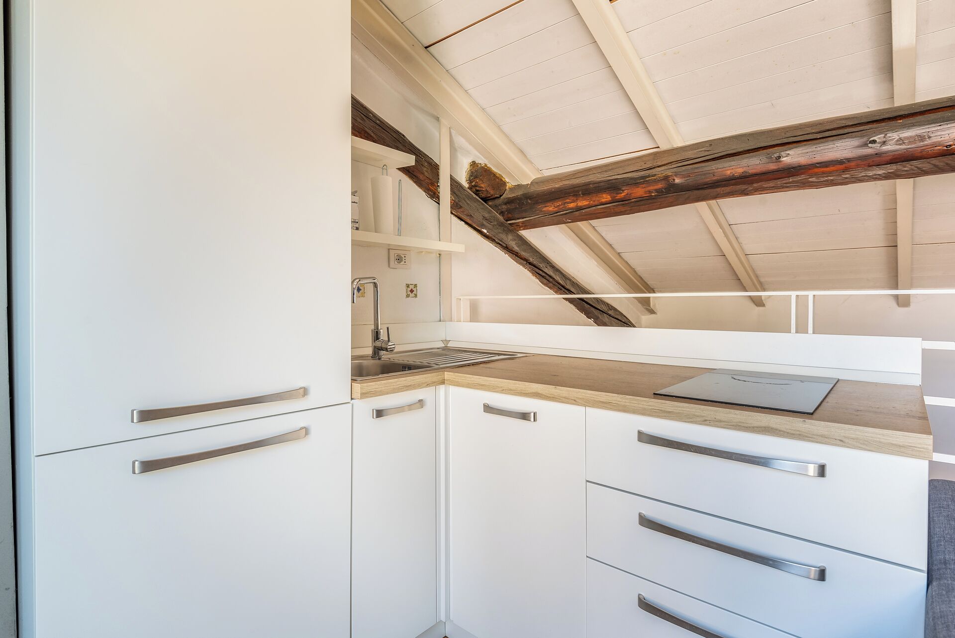 A kitchen with white cabinets, a wooden countertop, and a sloped ceiling with exposed beams.