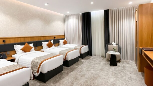 A hotel room with four beds, a desk, a chair, and a small table with a vase of flowers. - LECHAL (Madinah)