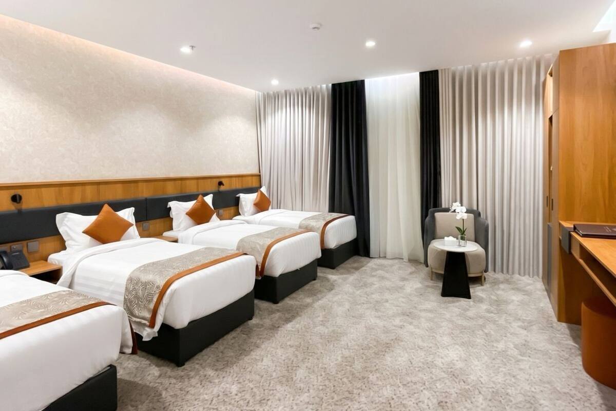 A hotel room with four beds, a desk, a chair, and a small table with a flower.