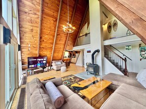 Een ruime loft met hoge plafonds, houten balken, een open haard, een televisie en een gezellige zithoek.