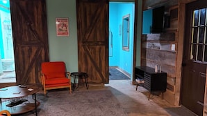 A rustic interior with a red chair, a small table, and a TV mounted on a wooden wall. - Romantic, peaceful Country getaway. 1-bedroom building with private Hot tub (Nashville)