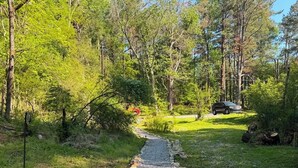 A gravel path bordered by rocks and grass, leading through a wooded area with trees and a parked car. - Romantic, peaceful Country getaway. 1-bedroom building with private Hot tub (Nashville)