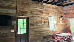 A rustic interior with exposed wooden beams, a ceiling fan, a dining area with red chairs, and a door with a window. - Romantic, peaceful Country getaway. 1-bedroom building with private Hot tub (Nashville)