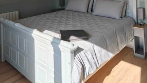 Quarto com teto inclinado, cama com cabeceira, mesa de cabeceira e luminária fixada na parede.