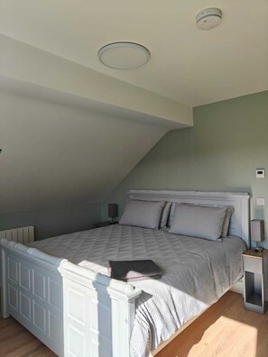 Ein Schlafzimmer mit schrägen Wänden, einem Bett mit Kopfteil, einem Nachttisch und einer Wandleuchte.