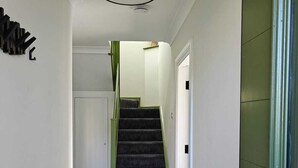 Um corredor com escada carpetada, radiador e porta com moldura verde.