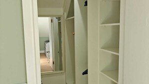 Um corredor estreito com assoalho de madeira que leva a um quarto com uma cama e uma porta.