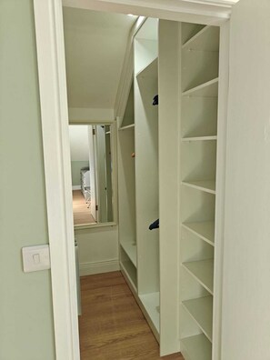 Ein schmaler Flur mit Holzboden führt zu einem Zimmer mit einem Bett und einer Tür.