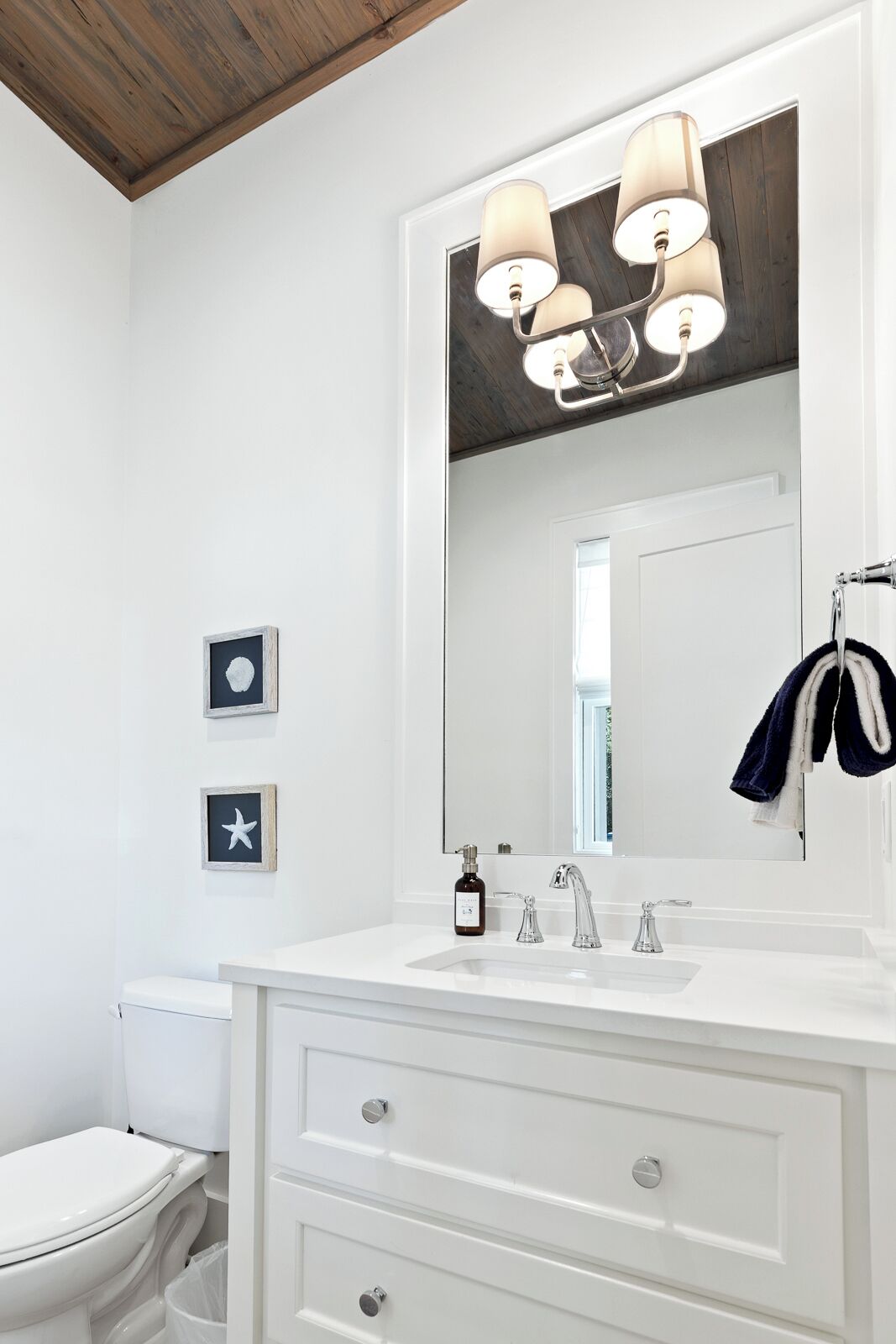 A bathroom with a white vanity, a large mirror, a wooden ceiling, and a towel rack.