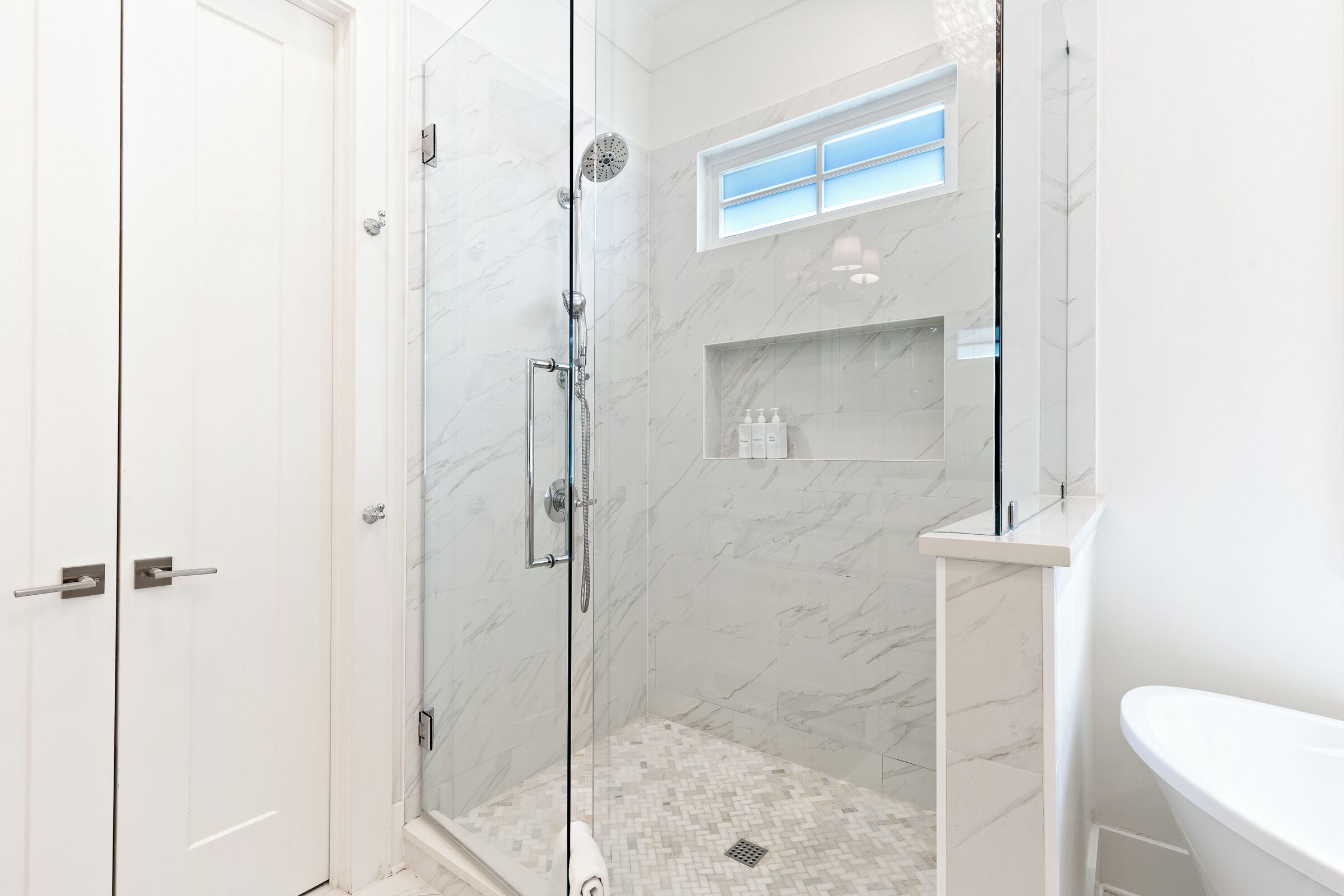 A modern bathroom with a glass-enclosed shower, a white sink, and a marble-tiled shower floor.