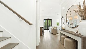 Een trap met houten treden en een leuning, die leidt naar een kamer met een grote spiegel, hanglampen en een bank.