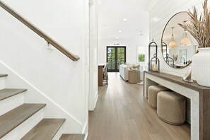 Una escalera de madera con barandilla que conduce a una habitación con un espejo grande, lámparas colgantes y un banco.