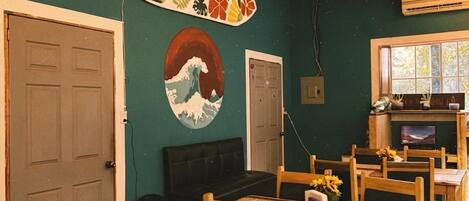 A room with a dining area, a surfboard art piece, a round painting, and a window with a view.