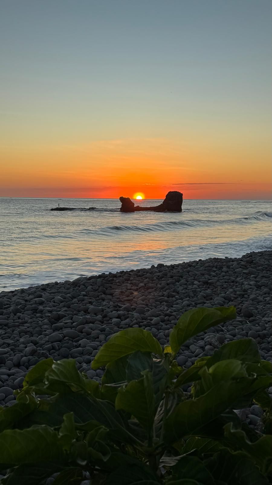 A sunset over a rocky beach with large boulders and calm water.