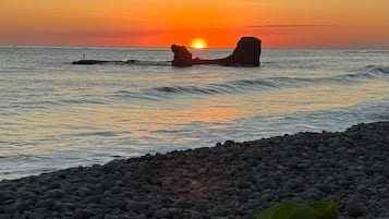 A sunset over a rocky beach with large boulders and calm water.