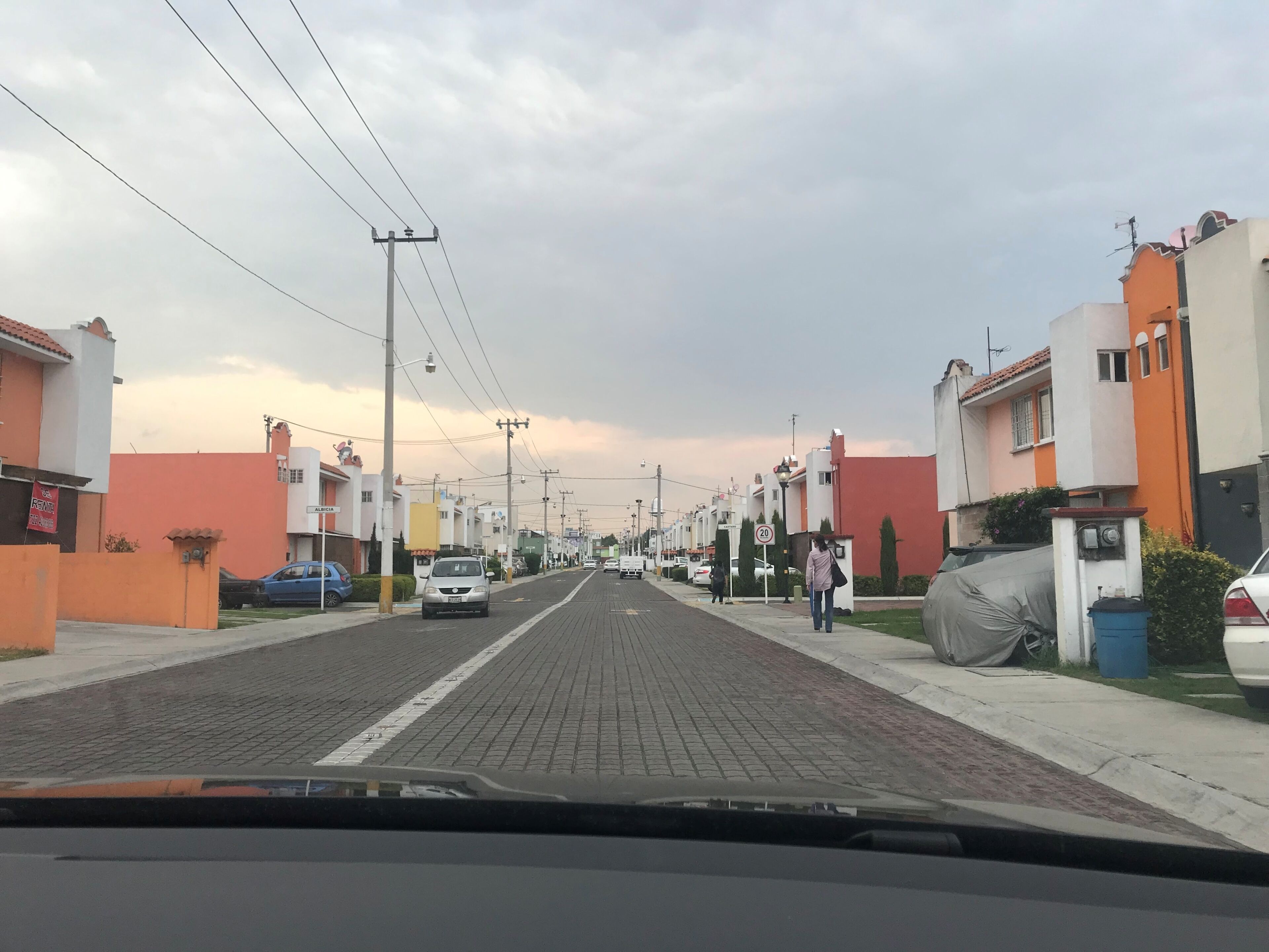 Une rue résidentielle bordée de maisons, un ciel dégagé et une personne qui marche.