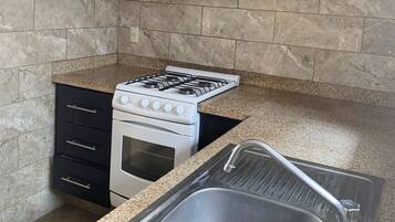 A kitchen with a gas stove, oven, black cabinets, granite countertop, and a stainless steel sink.
