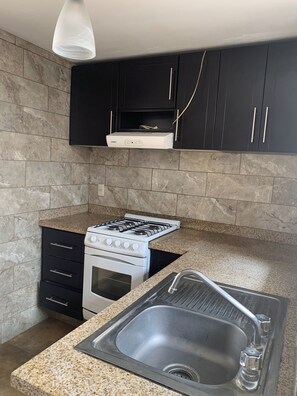 Eine Küche mit Gasherd, Backofen, schwarzen Schränken, einer Arbeitsplatte aus Granit und einer Spüle aus Edelstahl.