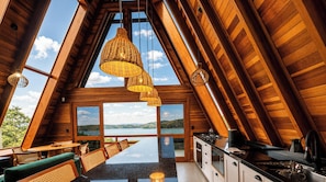 A modern, wooden interior with a kitchen, dining area, and large windows offering a scenic view.