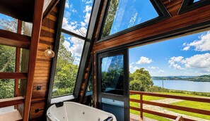 A modern cabin with a large glass window, a wooden deck, and a hot tub.