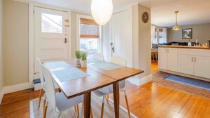 A dining area with a wooden table, white chairs, and a hanging light fixture. - Prime Location, Private Rooftop Deck.Walk to Old Port,waterfront, Museums& Music (Portland)