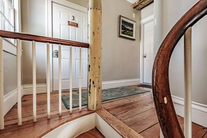 Eine Holztreppe mit weißen Balustern, einem Holzgeländer und einer grünen Fußmatte auf Holzdielen.