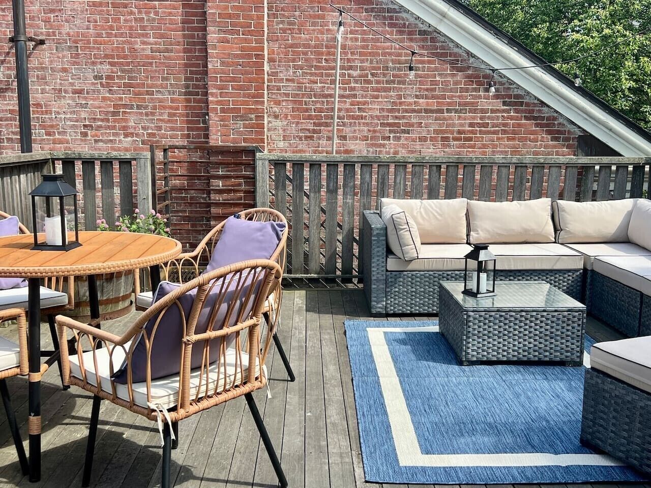 Une terrasse en bois avec des meubles en osier, un mur en briques et un tapis bleu.