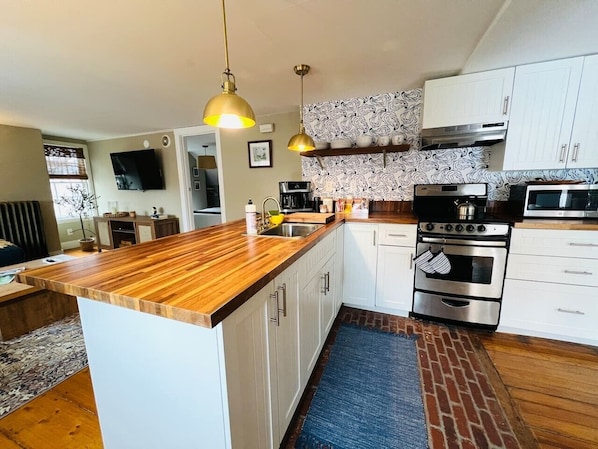 Una cocina moderna con una isla de madera, electrodomésticos de acero inoxidable, armarios blancos y un salpicadero decorado.