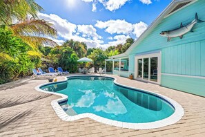 Ein Pool mit geschwungener Kante, umgeben von Liegestühlen und Sonnenschirmen, mit einem Gebäude, das eine große Fischverzierung an der Seite hat.