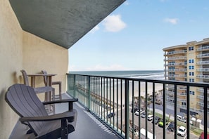 Ein Balkon mit Blick auf das Meer, ein Stuhl, ein Tisch und ein Gebäude gegenüber.